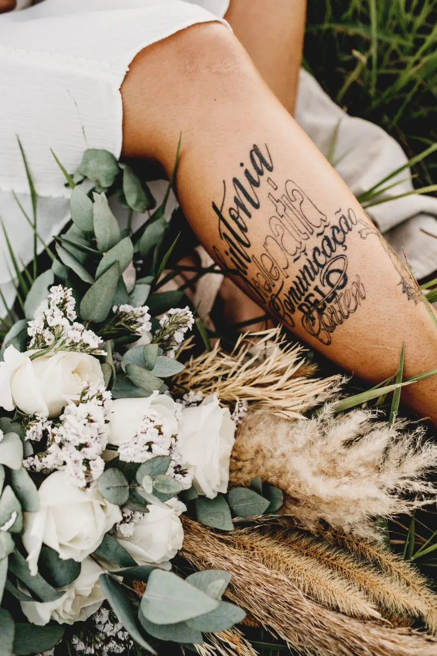 Lettrage calligraphié sur l'avant-bras, à côté d'un bouquet de fleurs blanches