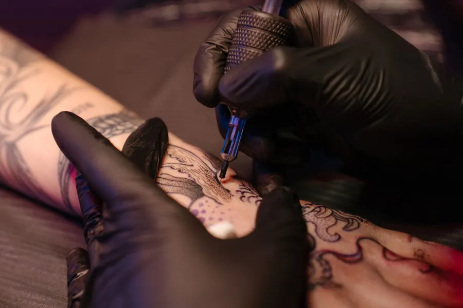 Mains gantées de noir qui tatouent un avant-bras, vue rapprochée