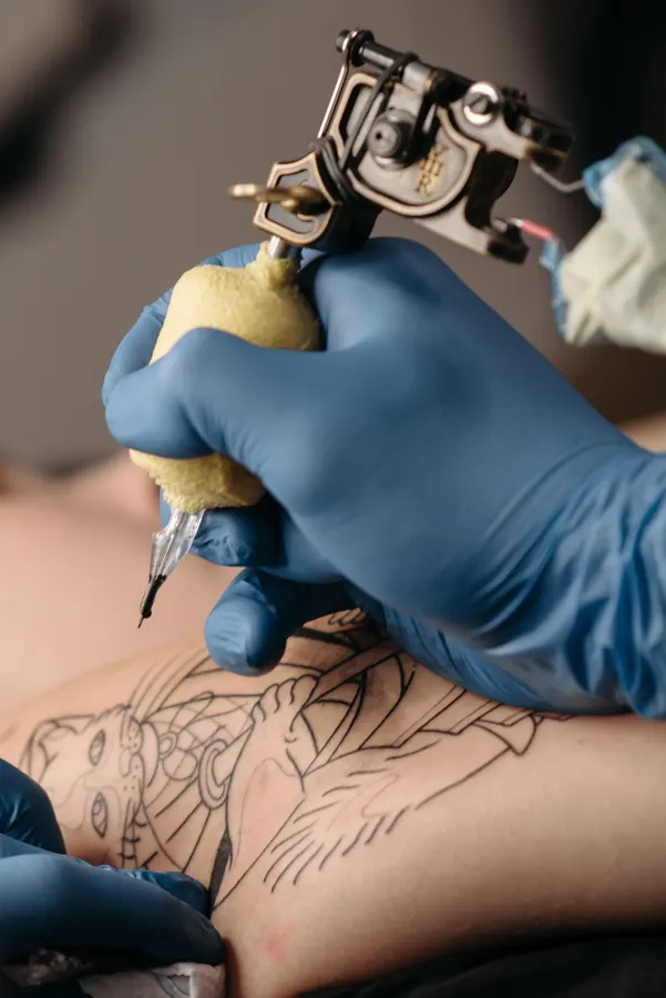 Mains en gants bleus qui tiennent une machine à tatouer pendant une séance