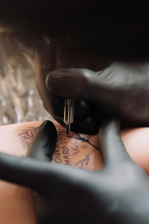 Lettrage manuscrit en train d'être tatoué, mains gantées de noir