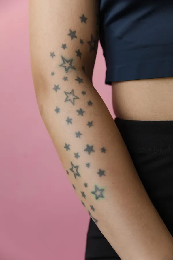 Traînée de petites étoiles tatouées le long d'un avant-bras, sur fond rose