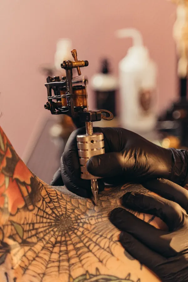 Toile d'araignée tatouée au milieu de motifs orange, machine dorée en main