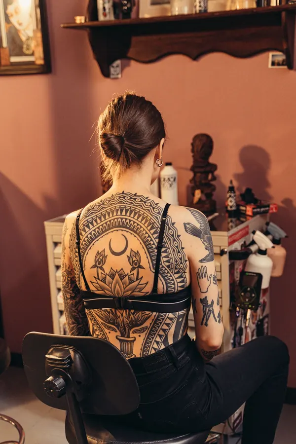 Une cliente de dos, assise dans un atelier de tatouage aux murs couverts de cadres