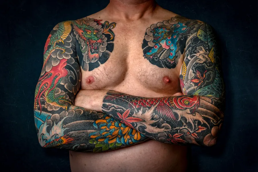 Bras croisés entièrement tatoués en couleurs vives sur fond sombre