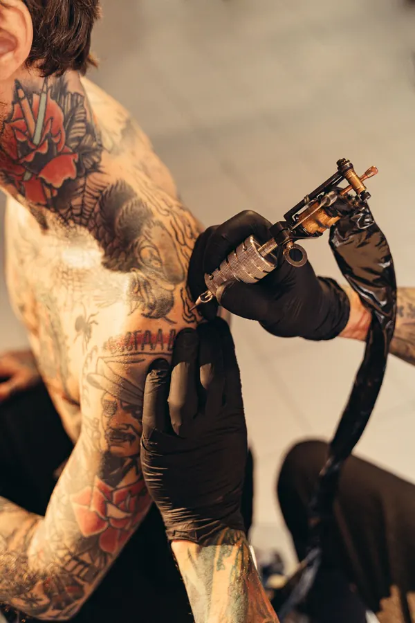Machine à tatouer en action sur un bras déjà couvert de roses rouges en couleur