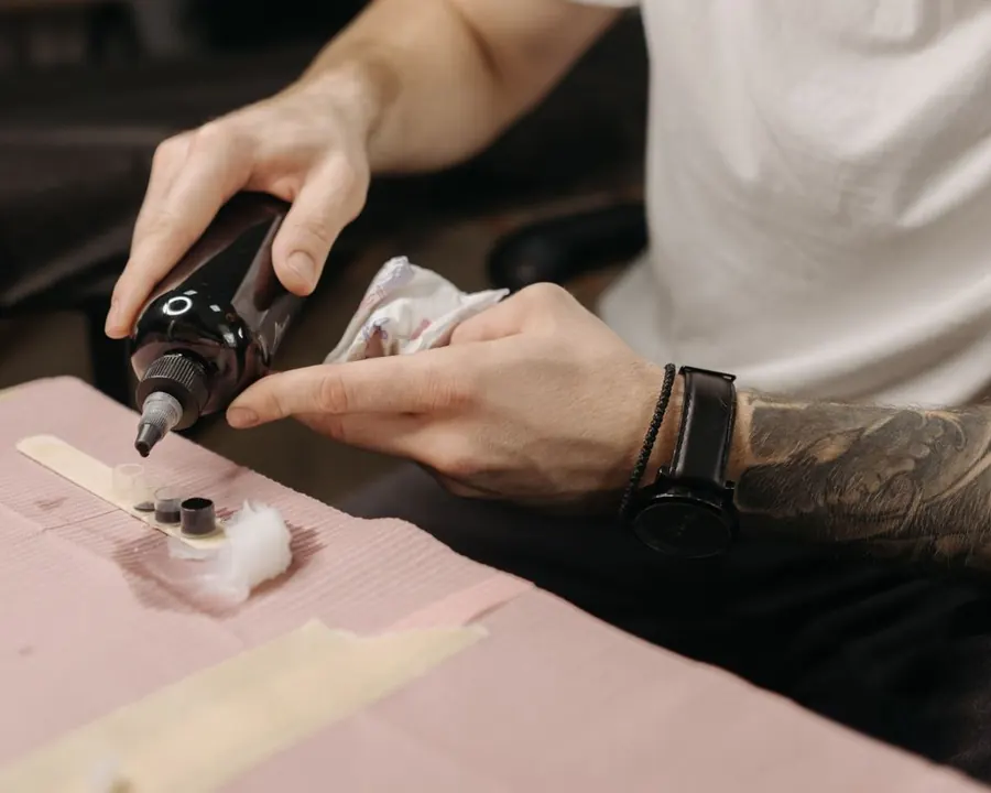 Des mains tatouées versent de l'encre dans de petites coupelles avant une séance.