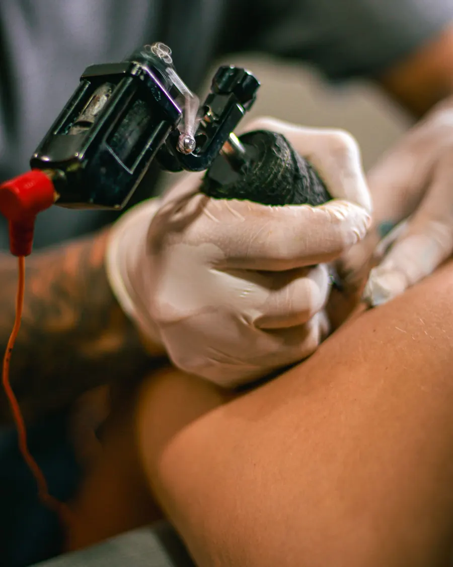 Gros plan sur des mains gantées qui tiennent une machine à tatouer pendant une séance.
