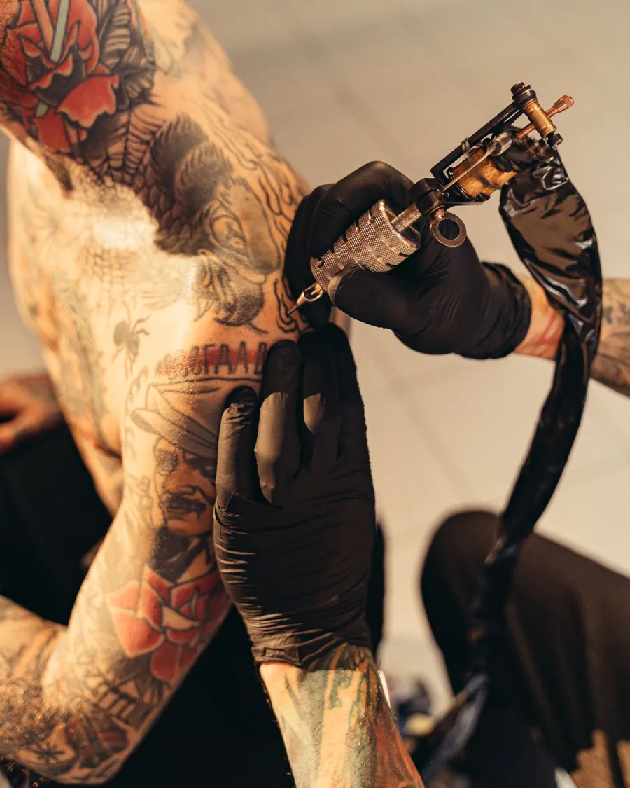 Un tatoueur aux bras tatoués travaille à la machine sur l'épaule d'un client.