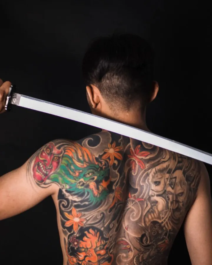 Dos entièrement tatoué : un dragon vert et des fleurs orangées parmi des nuages gris.