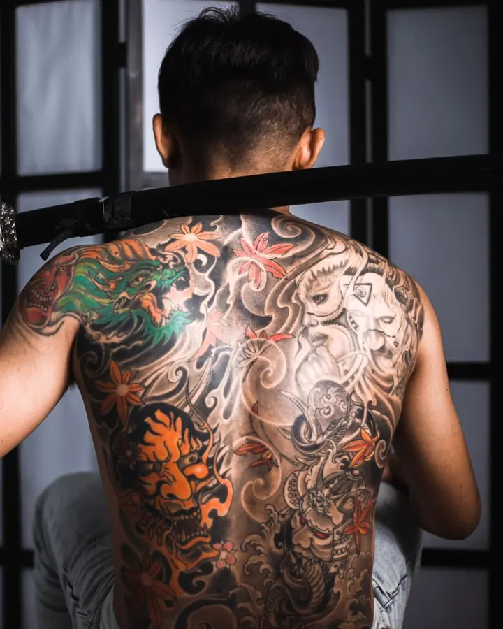 Grand dos irezumi en noir et gris, relevé d'un dragon vert sur l'épaule et de fleurs orange.