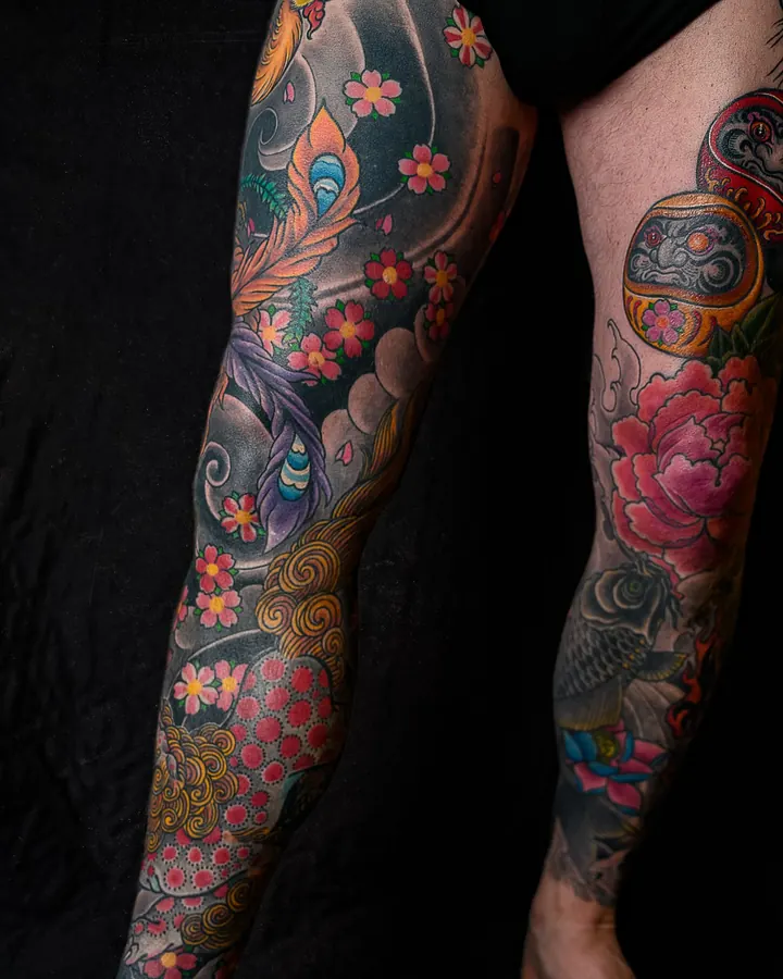 Deux jambes couvertes de pivoines roses, d'un phénix et d'un daruma dans un fond de nuages.
