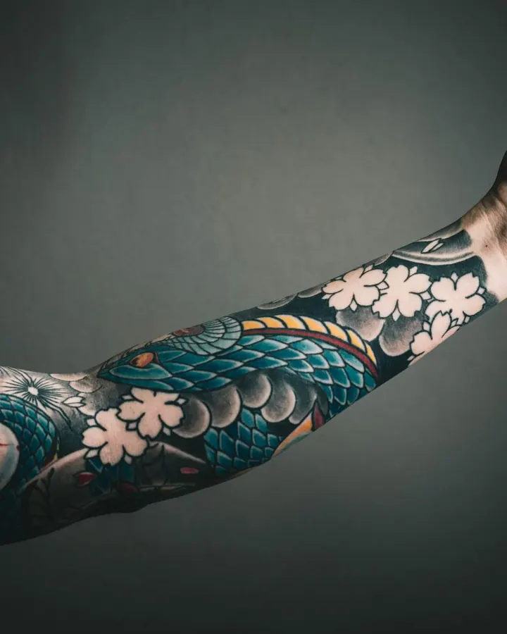 Bras tendu couvert d'un dragon bleu vert et de fleurs de cerisier blanches.