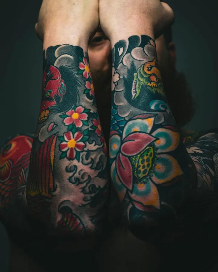 Deux avant-bras tatoués en couleur, avec des fleurs de lotus, des cerisiers et des vagues.