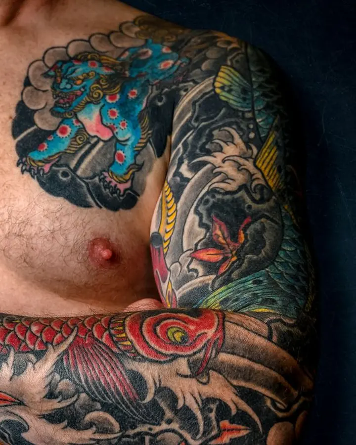 Poitrine tatouée d'un lion gardien bleu dans un cercle de nuages, prolongé par une manchette.