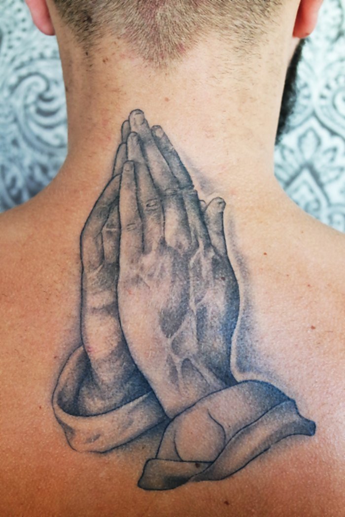 Mains en prière tatouées sur la nuque — pièce signature